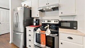 Cocina con refrigerador de acero inoxidable, cafetera, horno, microondas y alacenas blancas.