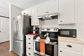 Eine Küche mit einem Edelstahl-Kühlschrank, einer Kaffeemaschine, einem Backofen, einer Mikrowelle und weißen Schränken.