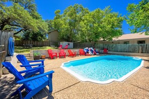 A backyard with a swimming pool, red and blue lounge chairs, and a wooden fence. - Tejas Hills Guest Haus #2 | Hill Country + Pool (Fredericksburg)