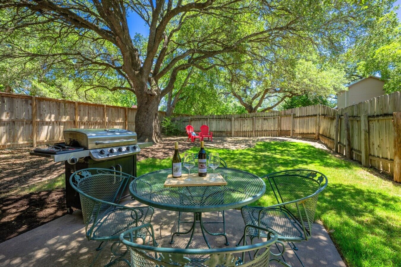 A backyard with a grill, a round table with chairs, and a wooden fence.