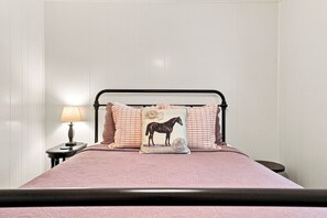A bed with a metal frame, pink bedding, and decorative pillows including one with a horse design. - Tejas Hills Guest Haus #1 | Near Main Street (Fredericksburg)