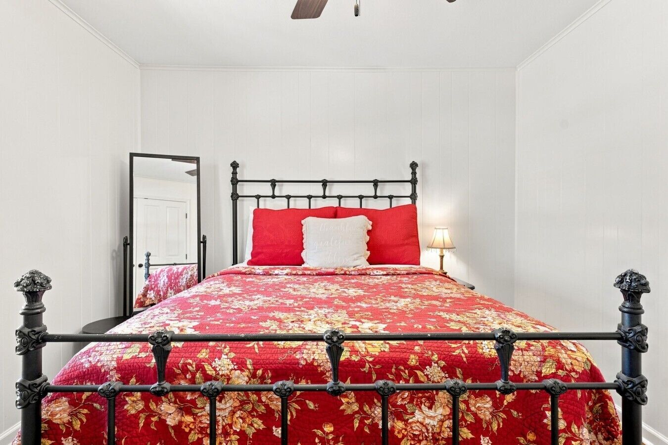 Ein Bett mit Metallgestell und Blumenmuster auf der Bettwäsche, eine Nachttischlampe und eine Tür im Hintergrund.