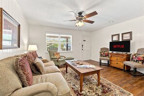 A living room with a sofa, armchairs, a coffee table, a television, and a ceiling fan. - Tejas Hills Guest Haus #1 | Near Main Street (Fredericksburg)