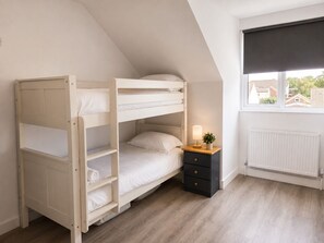 A room with a bunk bed, a bedside table with a lamp, and a window with a view of houses. - Modern 5BR Home | Sleeps 12 | Free Parking (Southampton)