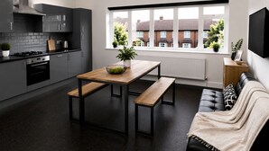 Eine moderne Küche mit Essbereich, einem schwarzen Ledersofa und einem Fenster mit Blick auf Häuser.