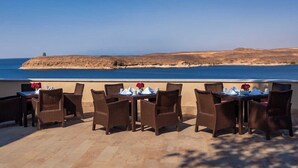 An outdoor dining area with wicker chairs and tables, overlooking a coastal landscape. - Retac Abu Simbel Nefertari Hotel (Abu Simbel)
