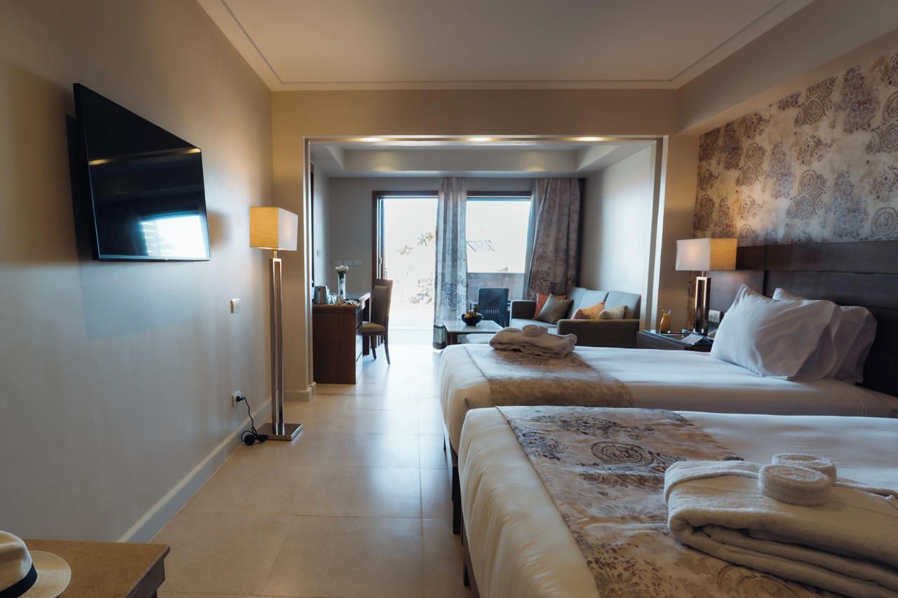 A hotel room with a bed, bedside table, lamp, and a television mounted on the wall.