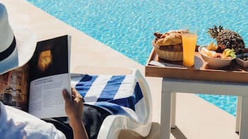 Alguém lendo um livro à beira da piscina, com uma bandeja de comida e bebidas.