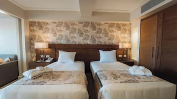 Quarto de hotel com duas camas, cabeceira de madeira, papel de parede estampado e um guarda-roupa.
