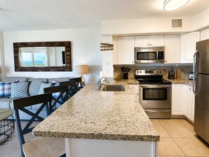 A modern kitchen with granite countertops, stainless steel appliances, and a dining area with a view. - The Fishing Shack | 2BR/2BA | Ocean Pointe 2312 (Tavernier)