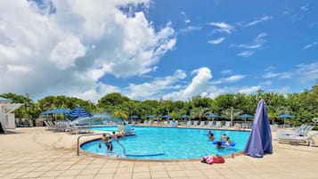 A swimming pool with lounge chairs, umbrellas, and palm trees.