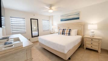 A hotel room with a bed, bedside tables, a desk with a phone, a ceiling fan, and a window with blinds.