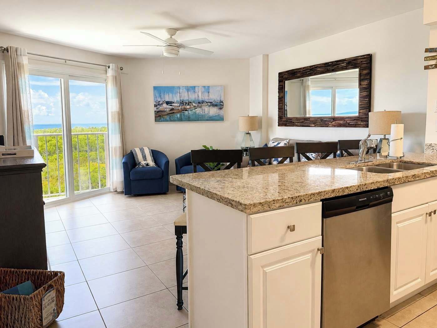 A modern kitchen with a central island, a dining area with chairs, a large window with a view, and a ceiling fan.