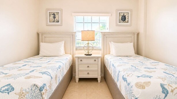 A bedroom with two beds, a nightstand with a lamp, and framed artwork on the walls. - Key Largo Resort 2bd/2bth Ocean Views (Tavernier)