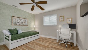 Une chambre à coucher comprenant un lit, un bureau, une chaise, un ventilateur de plafond et des œuvres d’art.