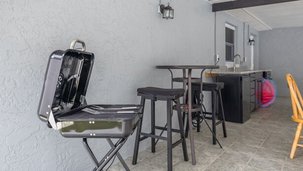 Un coin cuisine équipé d’un barbecue intégré, d’un tabouret de bar, d’une chaise haute et d’une chaise en bois.