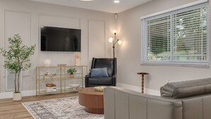 Un salon moderne avec un téléviseur à écran plat, un fauteuil en cuir noir, une table basse ronde et un canapé gris.
