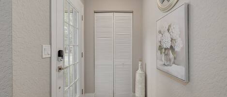 A hallway with a white door, a wall-mounted light fixture, and a framed picture of flowers.