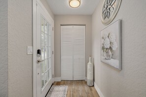 A hallway with a white door, a wall-mounted light fixture, and a framed picture of flowers. - Clearwater Pool Oasis -3 BR- 2 King Beds - Near Beach (Clearwater)