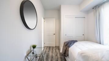 A bedroom with a bed, a round mirror, a small table with a plant, and a door leading to another room.