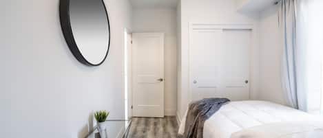 A bedroom with a bed, a round mirror, a small table with a plant, and a door leading to another room.
