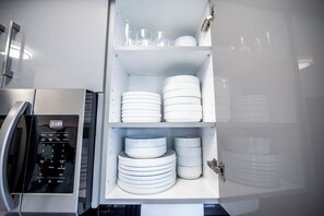 A kitchen with a microwave, a coffee machine, and a dish rack with stacked plates and bowls.