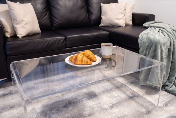 A clear glass coffee table with a plate of croissants and a cup of coffee.