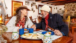 Una pareja sentada en una mesa de madera con un plato de comida, tazas azules y una tetera.