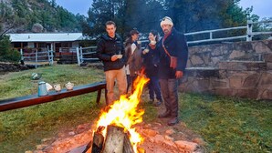 Un grupo de personas alrededor de una fogata, con un edificio rústico al fondo.