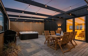 An outdoor patio with a hot tub, wooden deck, and a table with chairs. - Beautiful home in Løkken with sauna (Løkken)