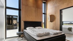 Ein modernes Schlafzimmer mit einem großen Bett, einem runden Spiegel und Blick durch eine Glastür.