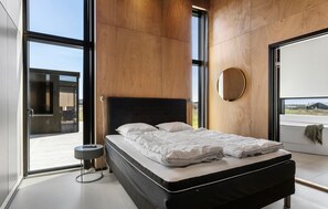 Ein modernes Schlafzimmer mit einem großen Bett, einem runden Spiegel und Blick durch eine Glastür.