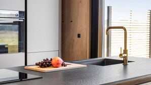 Eine moderne Küche mit Einbauofen, Holztür und Spüle aus Edelstahl mit goldfarbenem Wasserhahn.