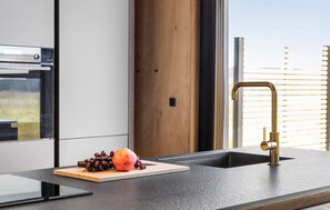 Eine moderne Küche mit Einbauofen, Holztür und Spüle aus Edelstahl mit goldfarbenem Wasserhahn.