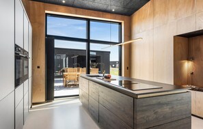 A modern kitchen with a large island, wooden cabinetry, and a view of the outdoors. - Beautiful home in Løkken with sauna (L økken)