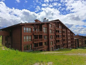 Ein mehrgeschossiges Gebäude mit Balkonen und einer flachen Dachterrasse, bewölkter Himmel.