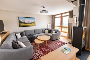 Ein modernes Wohnzimmer mit einem Ecksofa, einem runden Couchtisch, einem Kamin und einem großen Fenster mit Vorhängen.