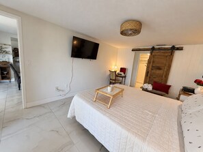 A hotel room with a bed, a TV mounted on the wall, a wooden door, and a small table with a tray. - Memories!! (Holiday)