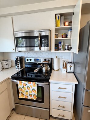 Cozinha compacta equipada com micro-ondas, fogão, forno e um balcão pequeno com torradeira.