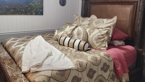 Een slaapkamer met een bed, een bankje, een plafondventilator, een wandklok en een lijst met een landschapsafbeelding.