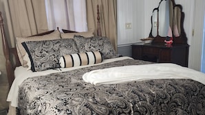 Een slaapkamer met een groot bed, een houten hoofdbord, een dressoir met spiegel en beige gordijnen.