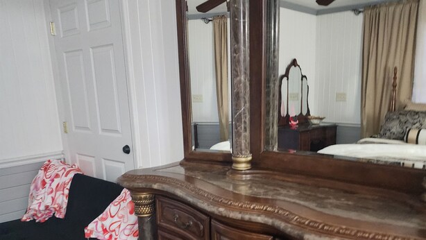 Een slaapkamer met een houten dressoir, een bed met een decoratieve spreideken, een plafondventilator en een deur.