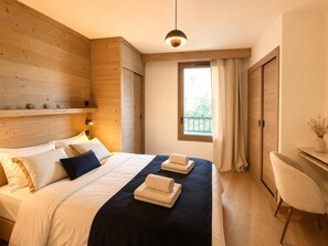 A hotel room with a bed, a desk, a chair, a window with curtains, and a hanging light fixture. - 10m from ski slopes, 1st floor, fitness, swimming pool, sauna, hammam, terrace, parking, tv (Huez)