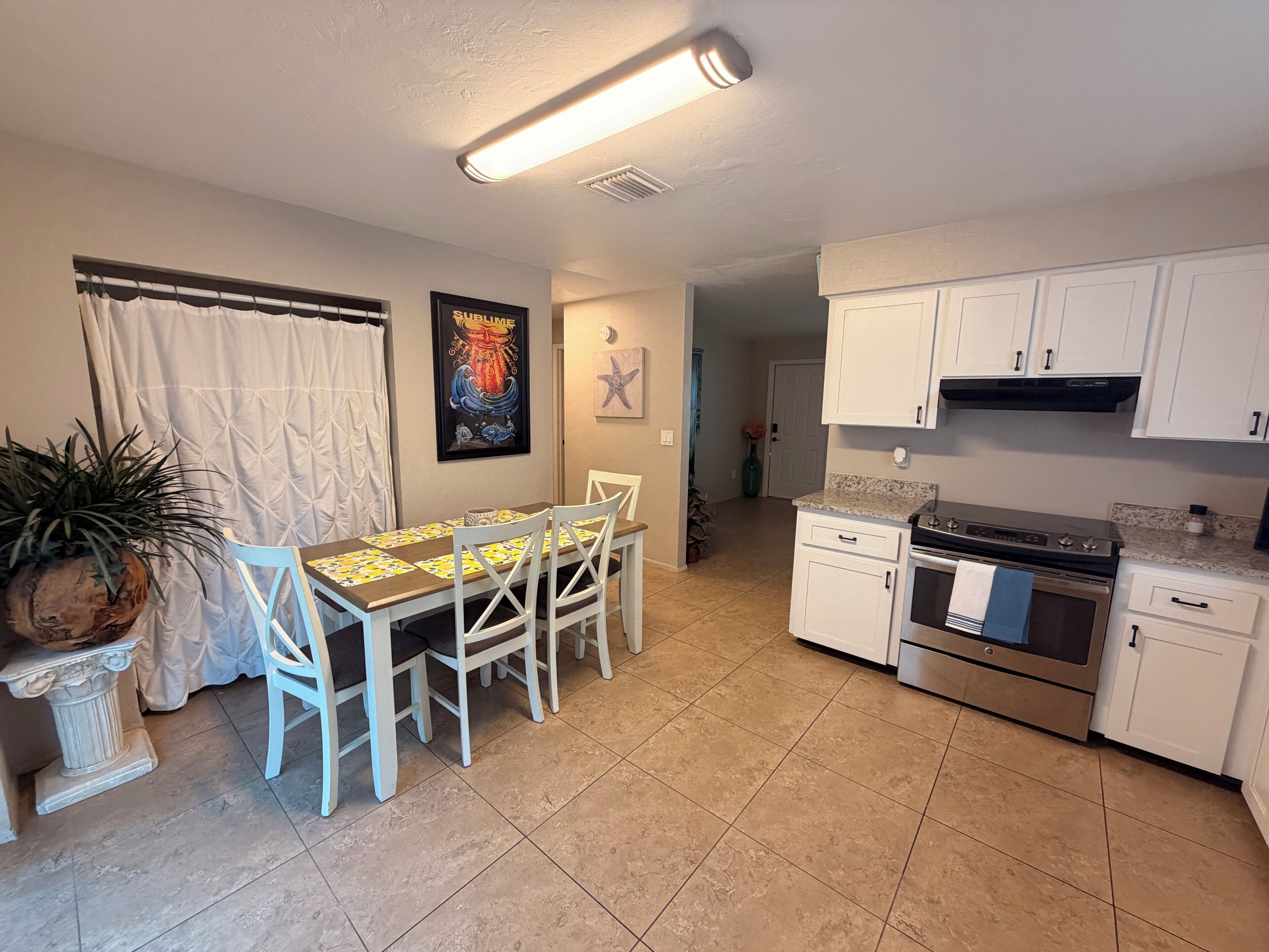 A compact kitchen with white cabinets, a dining table with chairs, and a tiled floor.