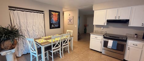 A compact kitchen with white cabinets, a dining table with chairs, and a tiled floor.