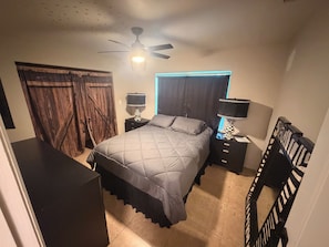A bedroom with a bed, two bedside tables, a ceiling fan, a window with curtains, and a wooden door. - Cozy 2-bedroom house just minutes from Sanibel and Fort Myers Beach! (Fort Myers)