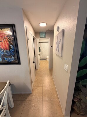A hallway with a framed picture, a ceiling light, a door leading to a bathroom, and a wall-mounted starfish decoration. - Cozy 2-bedroom house just minutes from Sanibel and Fort Myers Beach! (Fort Myers)