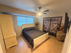 Ein Schlafzimmer mit einem Bett, einem Deckenventilator, einem Fenster mit Jalousien und einer Zierhaustür.