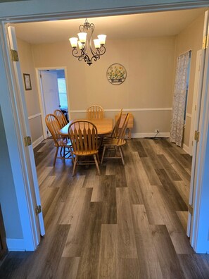 A dining area with a wooden table and chairs, a chandelier, and a welcome sign on the wall. - Nice 5-bedroom renovated farmhouse,  with A-C, 1.6miles/5 min to beaches (South Haven)