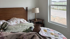 A bedroom with a wooden headboard, a bedside lamp, a window with a view, and a chandelier.